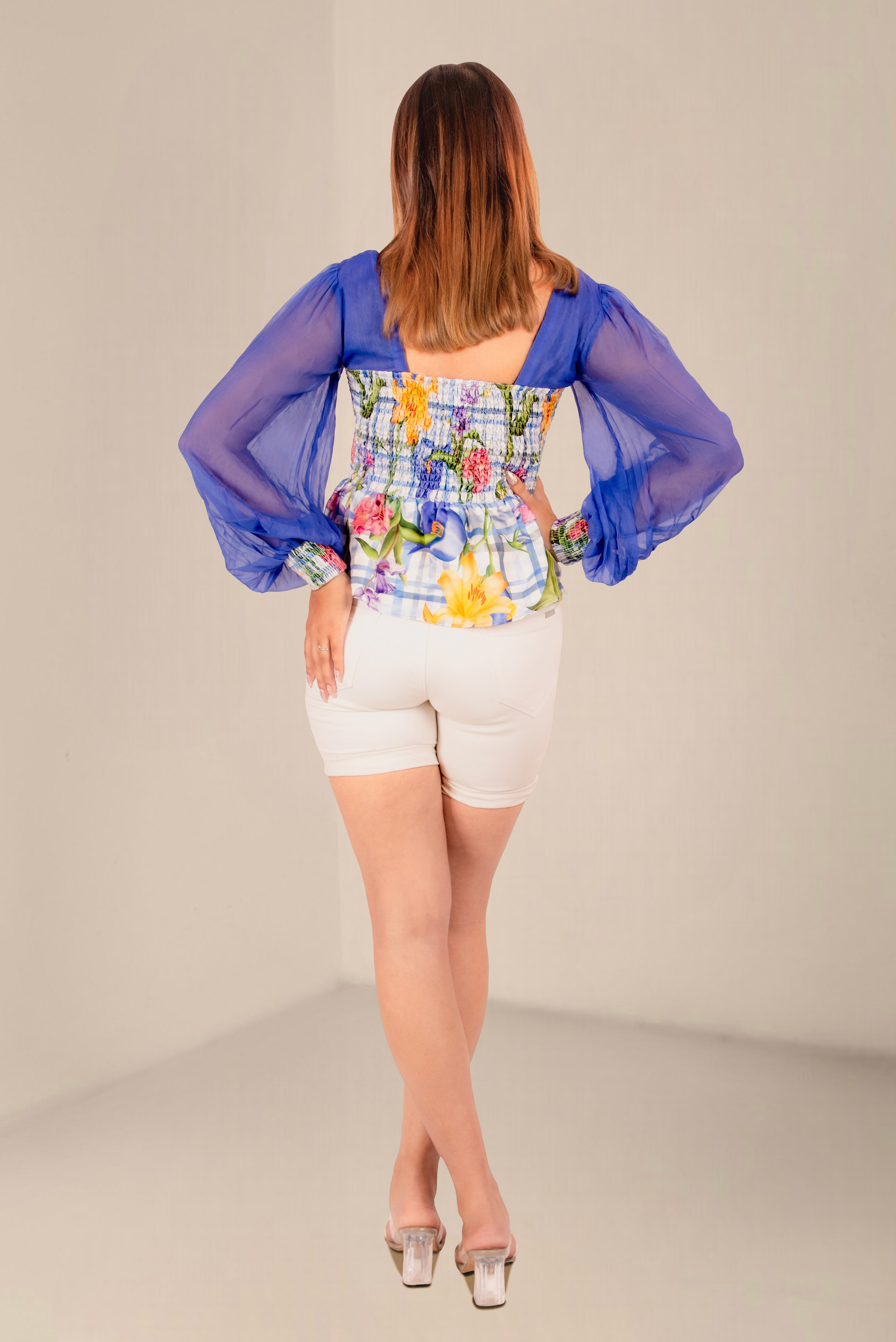 Woman wearing a colorful floral top and white shorts on a plain background